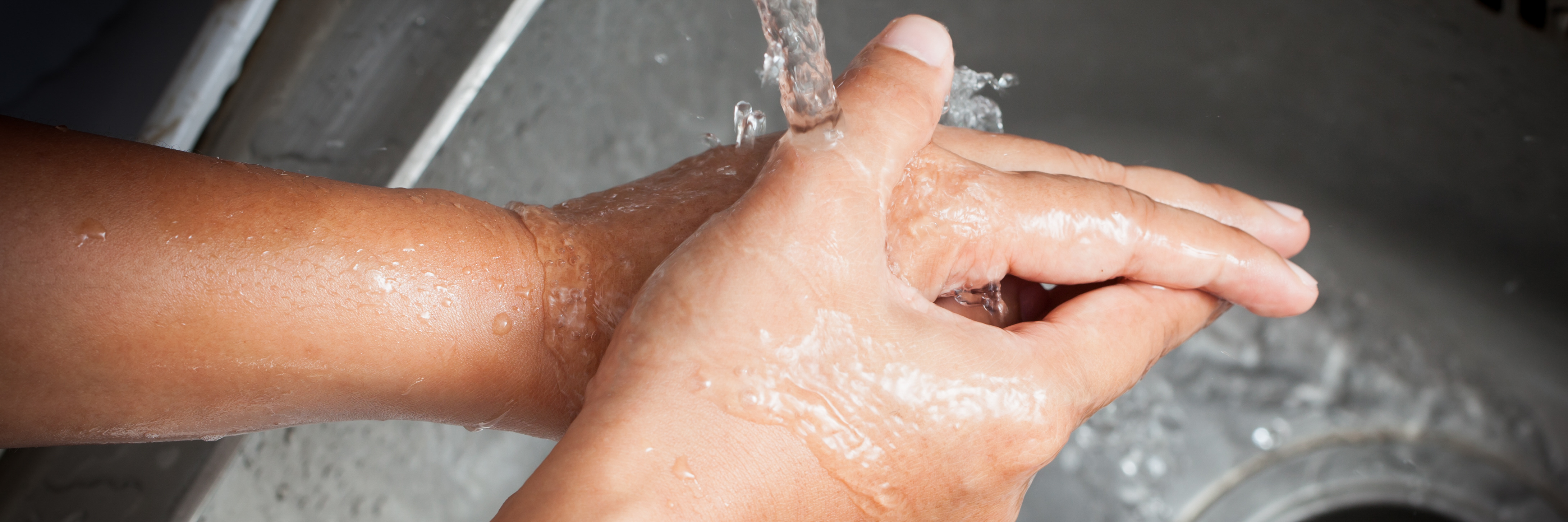 Auf dem Bild sieht man zwei Hände, die unter dem Strahl eines Wasserhahns gewaschen werden.