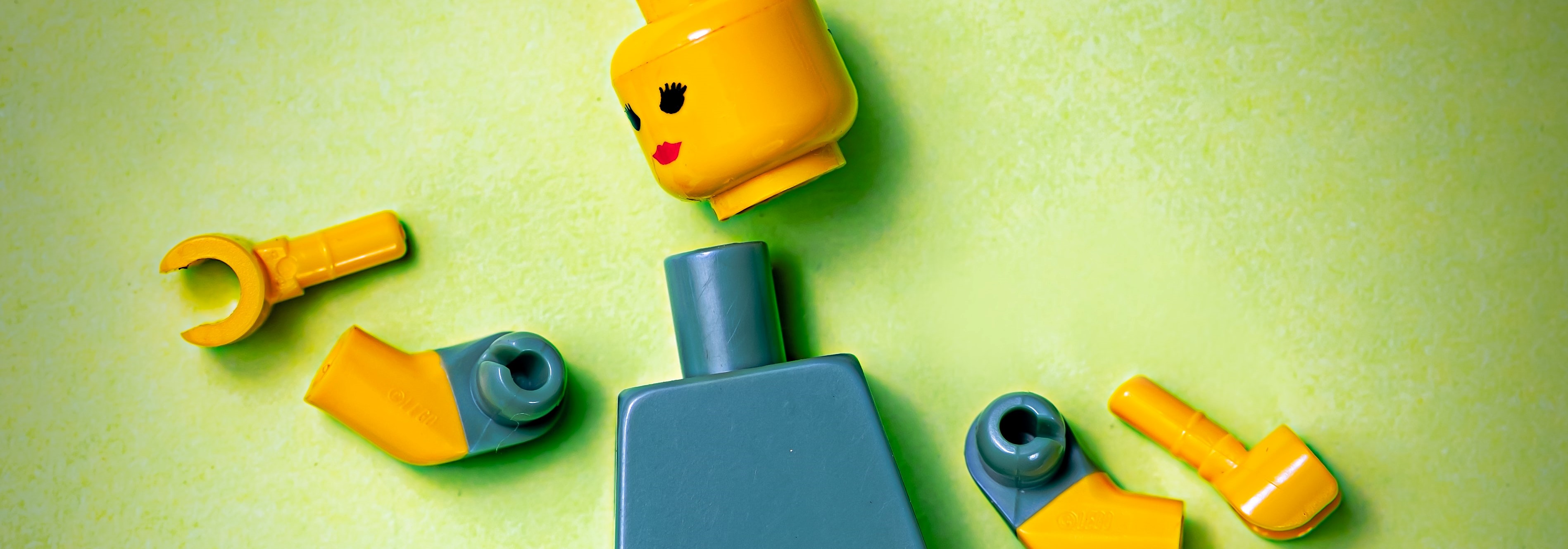 Das Bild zeigt ein in seine Einzelteile zerlegtes Lego-Männchen vor grünem Hintergrund.