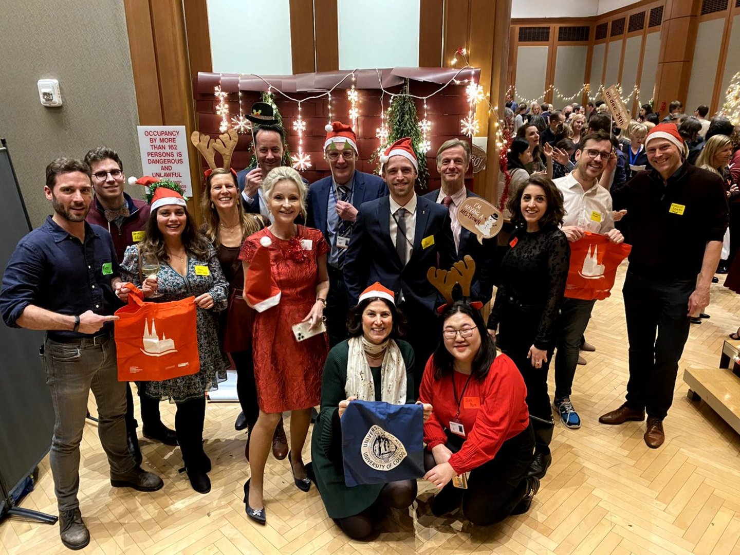 A group of people at a Christmas celebration holding Cologne tote bags and wearing Santa hats