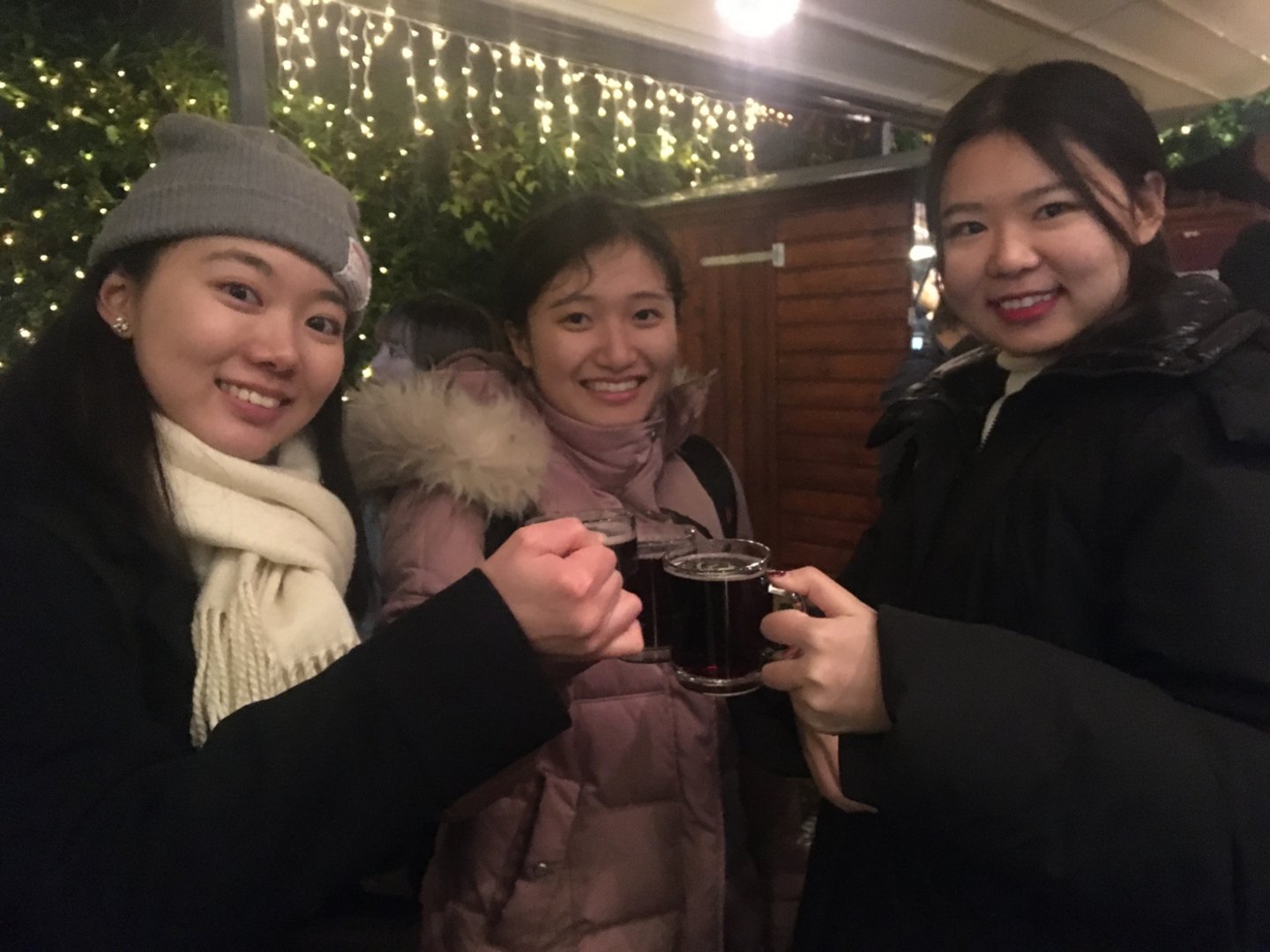 Three female students clink "Glühwein"-glasses on the christmas market