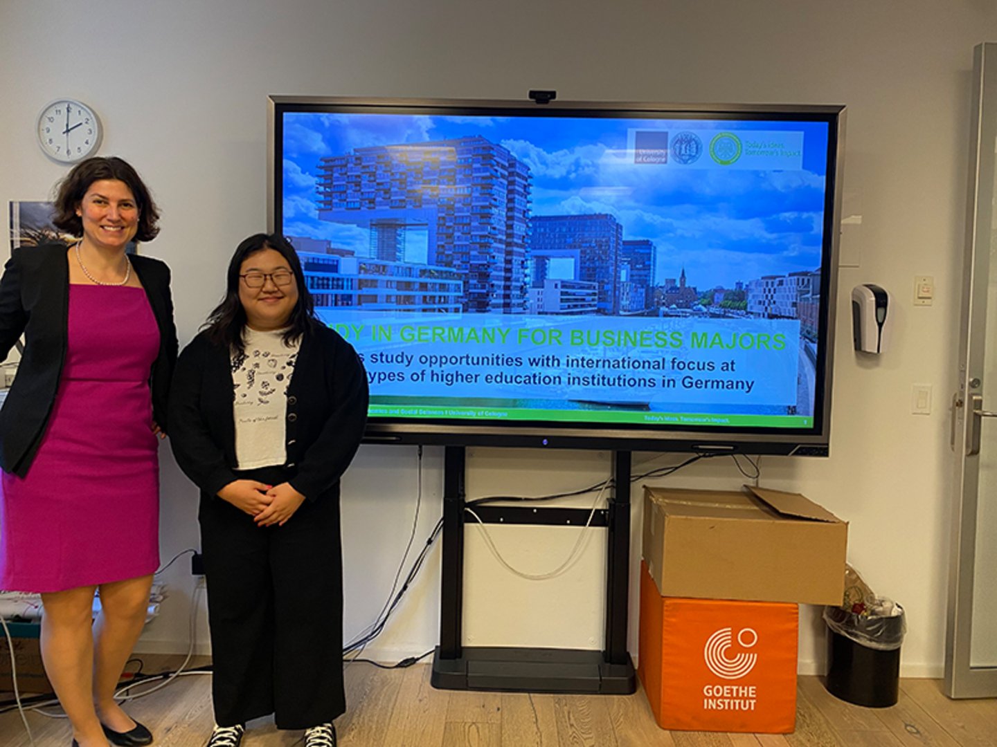 Two women standing in front of a monitor showing a presentation on Studying in Germany for Business Majors