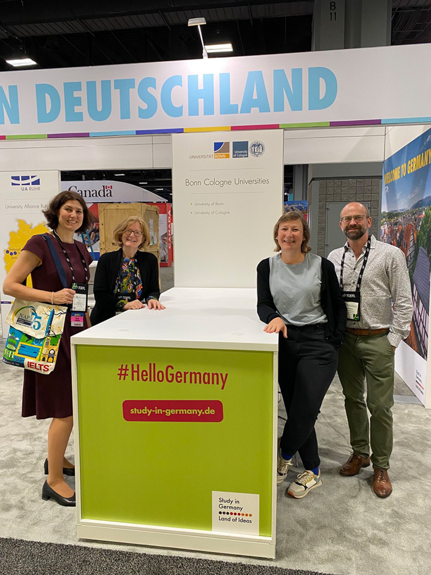 Four people standing at a conference booth that reads #HelloGermany