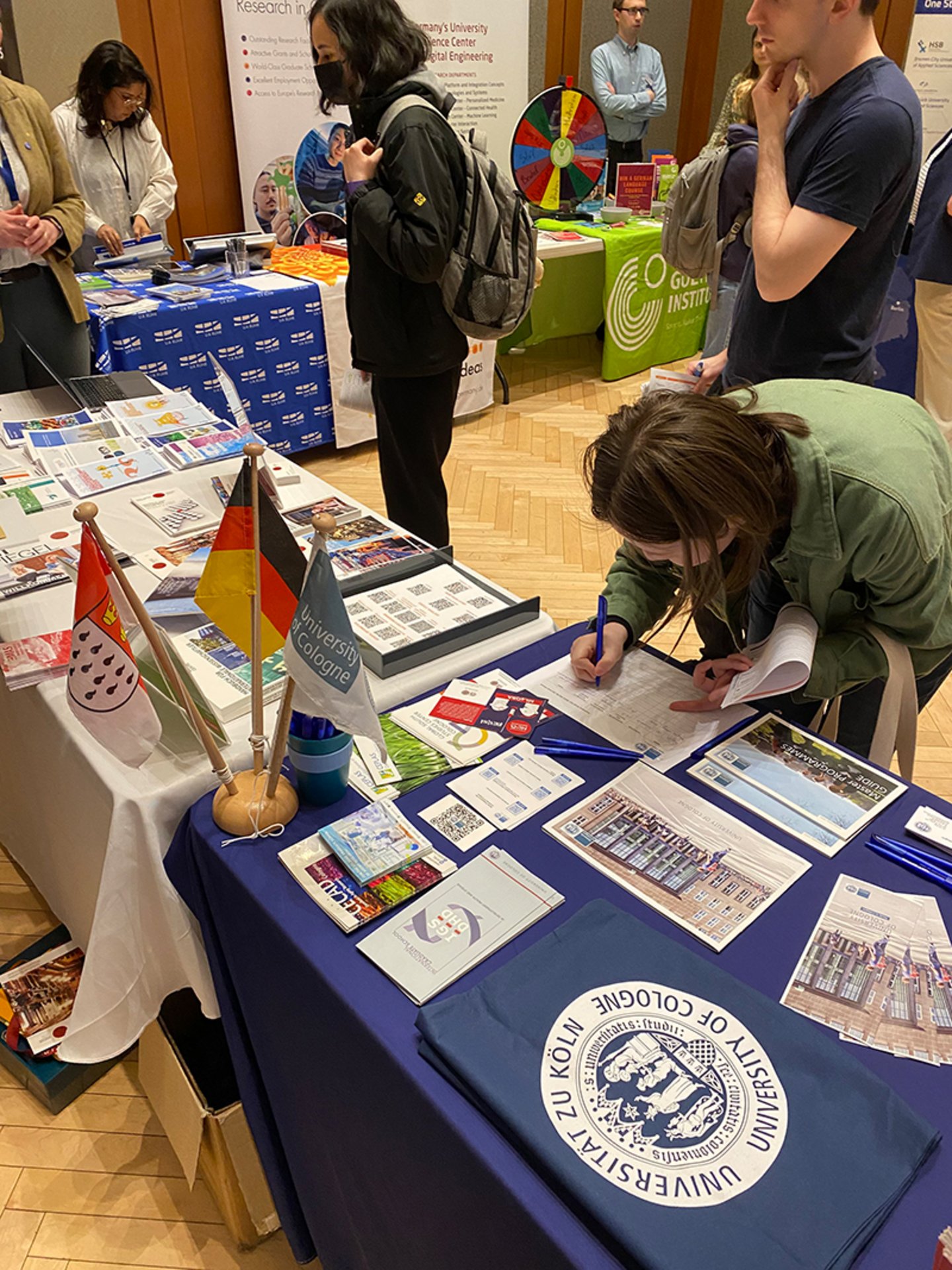 A student signing their name into a contact list at the University of Cologne booth