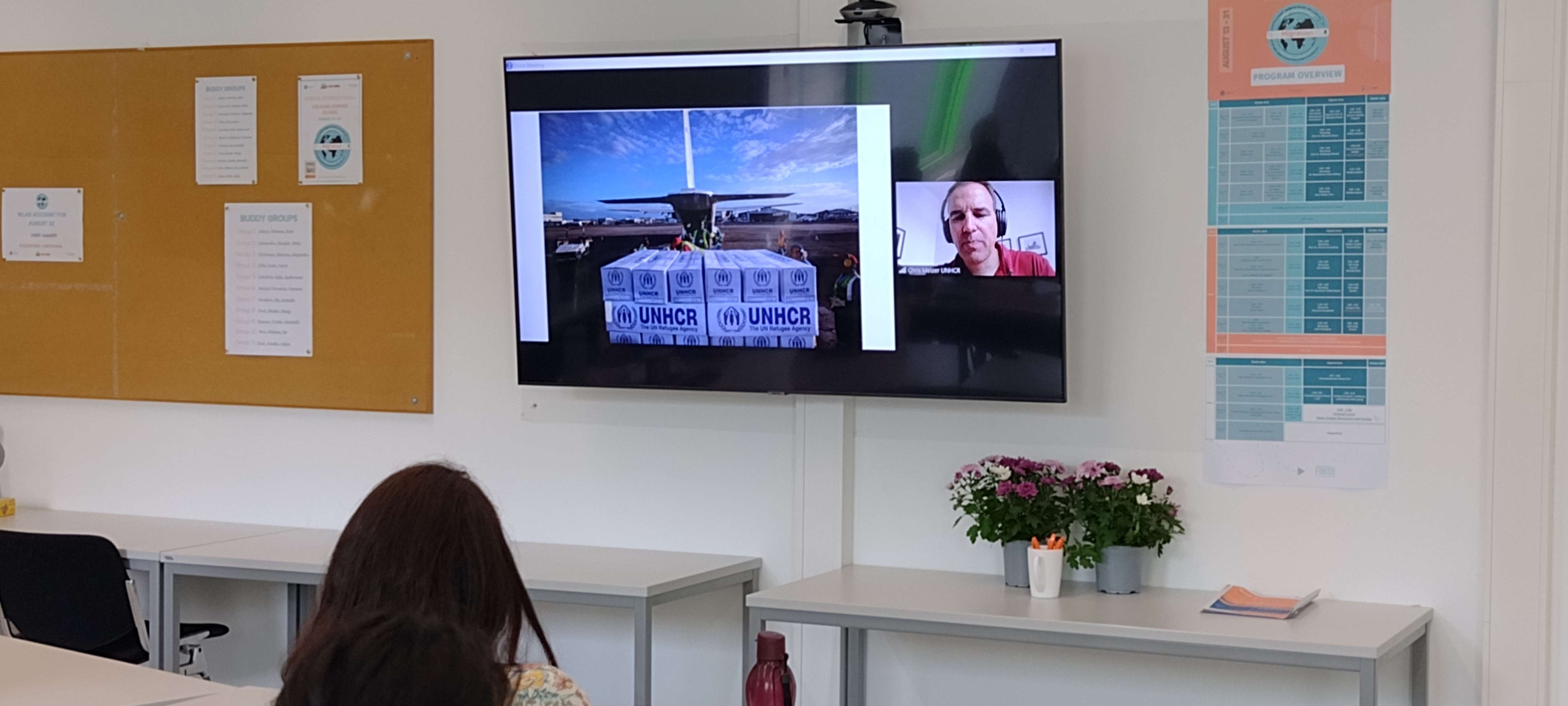Cologne Summer School on Migration / hybrid lecture with Chris Melzer showing him on a big TV screen in front of the onsite group