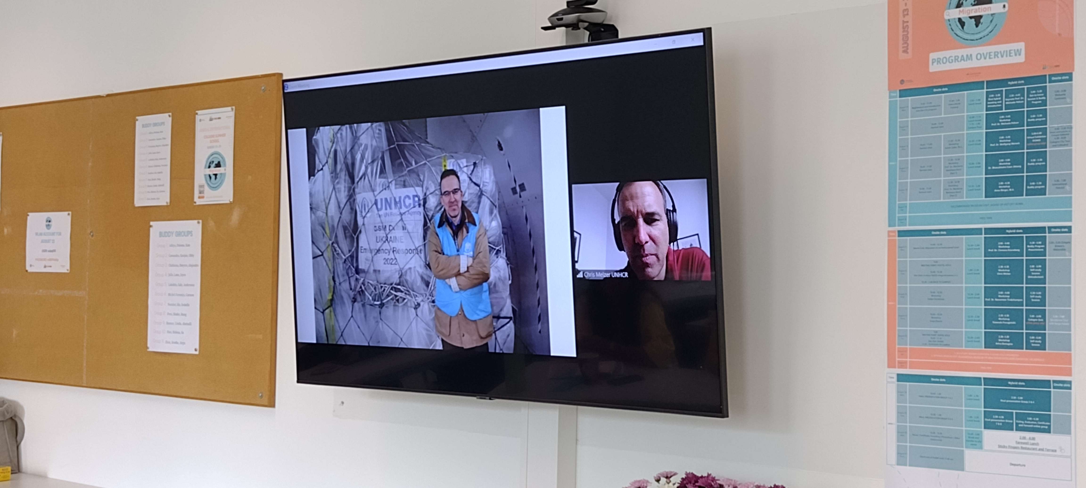 Cologne Summer School on Migration / hybrid lecture with Chris Melzer showing him on a big TV screen in front of the onsite group