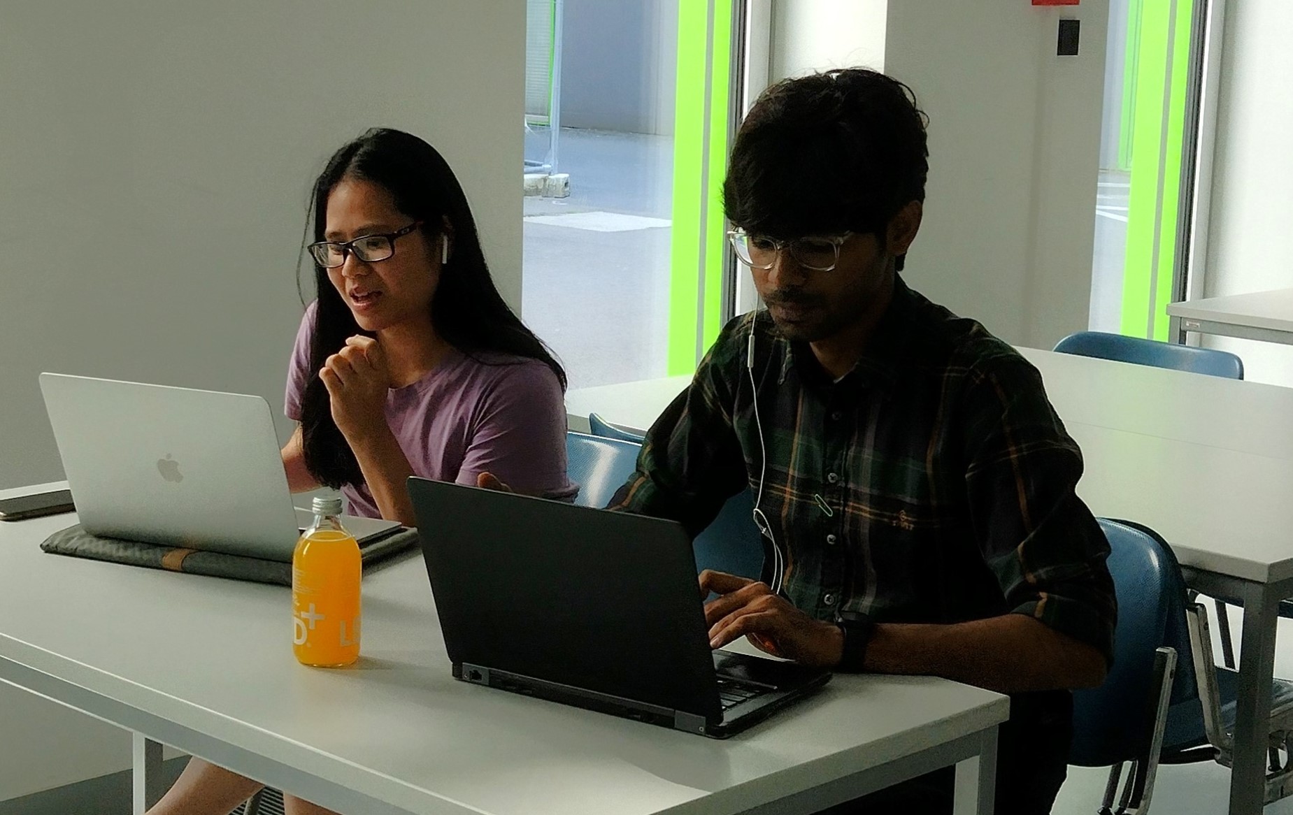 Two oniste buddies sitting next to each other and zooming with an online participant with their laptops