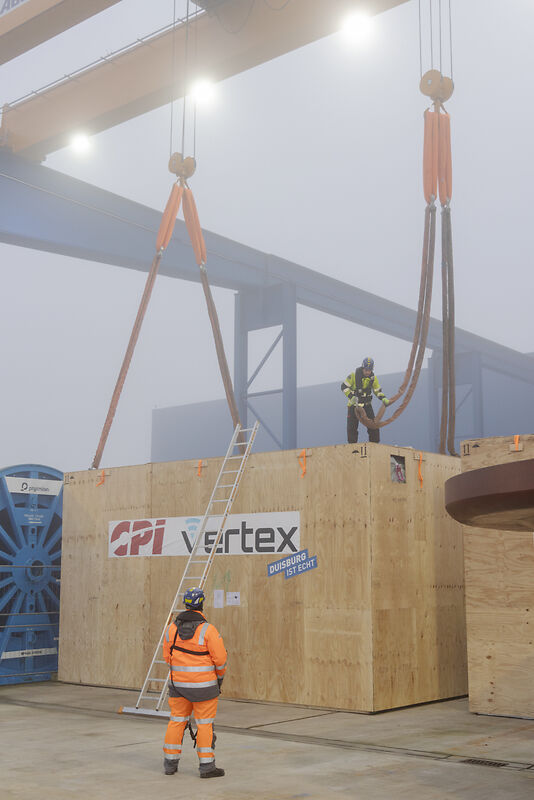 Ein Mann steht vor dem Container, der an Riemen hängt und koordiniert das Verladen